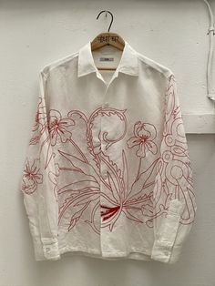 a white shirt with red flowers is hanging on a hanger in front of a wall