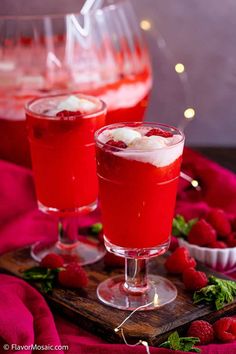 two glasses filled with liquid sitting on top of a wooden tray next to strawberries