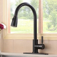 a black kitchen faucet next to a window with flowers in the vase on the counter