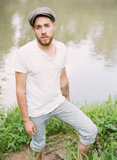 a man standing in front of a body of water wearing a hat and sweatpants