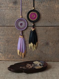 three pieces of jewelry hanging on a wooden wall next to a tray with beads and chains