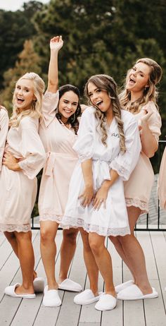 bridesmaids in pink robes and white slippers posing for the camera with their arms up