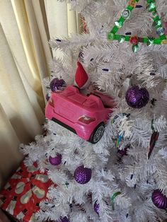 a pink toy car sitting on top of a white christmas tree