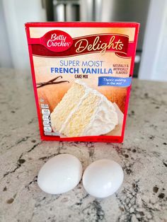 two white eggs sitting next to a carton of cake mix on a counter top