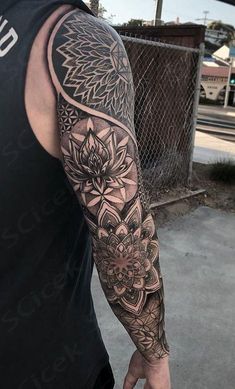 a man with a black and white tattoo on his arm is standing in front of a fence