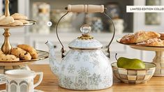 a tea kettle sitting on top of a wooden table filled with pastries and desserts