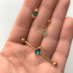 a person is holding two different types of piercings in their hand, one with green stones on it