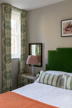 a green headboard on a bed in front of a window with curtains and a lamp