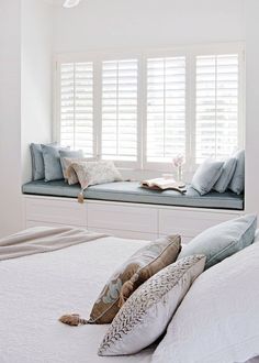 a bedroom with white walls and pillows on the bed, along with a window seat