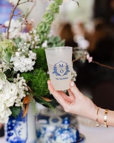 a woman holding up a glass with flowers in it on a table next to other vases