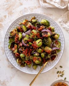 a white plate topped with brussel sprouts and onions next to a bowl of sauce