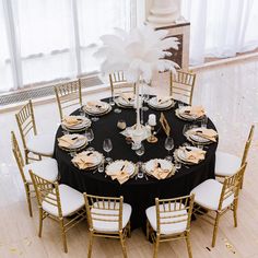 a table set up for an event with white and gold decorations, black linens and feathers