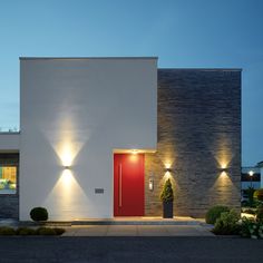 a modern house with red door and lights on the side