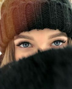 a woman with blue eyes wearing a black hat and fur pom - pom