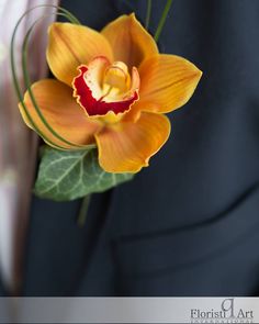 a man in a suit holding a yellow and red flower with green leaves on it