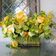 a vase filled with yellow and green flowers on top of a table next to a mirror