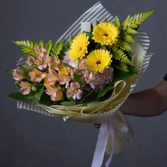 a person holding a bouquet of yellow and pink flowers with green leaves on the stems