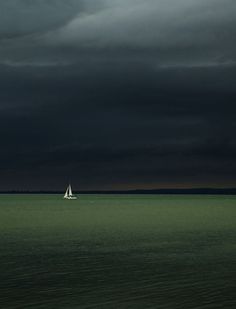 a lone sailboat in the distance under a dark sky