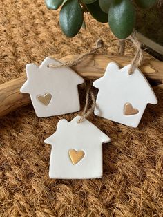 three white ceramic houses with gold hearts hanging from the front and side on a tree branch