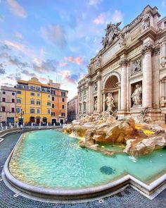 a large fountain in front of a building with statues on the sides and people standing around it