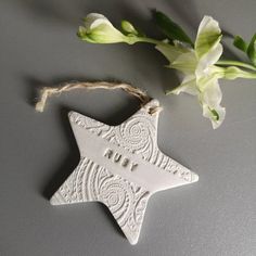 a white ceramic star ornament hanging from a string next to flowers on a table