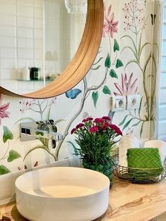 a bathroom sink sitting under a mirror next to a wooden counter top with flowers on it