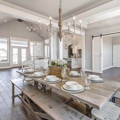 a dining room table with white plates and silverware on it, in the middle of a large open floor plan