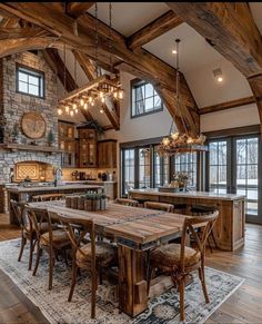 a large dining room table with chairs and lights hanging from the ceiling in front of an open kitchen area