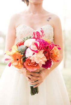 a woman in a wedding dress holding a bouquet of flowers and looking at the camera