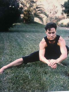 a man sitting in the grass with his hands on his knees and looking at the camera