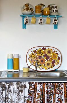 a kitchen counter with dishes and cups on the shelf above it is decorated with sunflowers