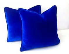 two blue velvet pillows sitting on top of a white bed next to eachother