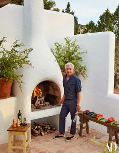 a man standing in front of an outdoor pizza oven with firewood on the side