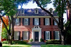 a red brick house with black shutters and trees