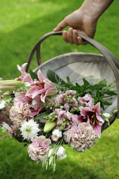 a person holding a basket filled with flowers on top of a grass covered park field