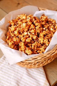 a basket full of caramel popcorn sitting on top of a wooden table next to a white towel