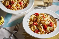 two white bowls filled with pasta on top of a blue and yellow table cloth next to silverware