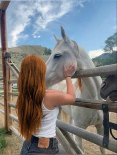 a woman petting a white horse behind a fence