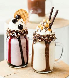 two glasses filled with milkshakes sitting on top of a wooden table next to each other