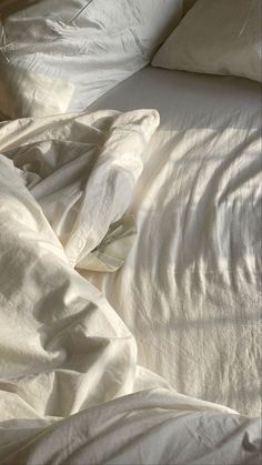 an unmade bed with white sheets and pillows