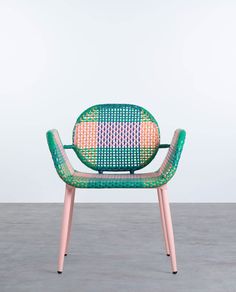 a green and pink chair sitting on top of a cement floor next to a white wall