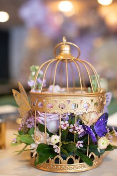 a birdcage filled with flowers and butterflies on top of a table