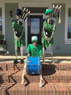 three skeletons in green and white outfits are playing drums on the front steps of a house