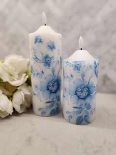 two blue and white candles sitting next to each other on a table with flowers in the background