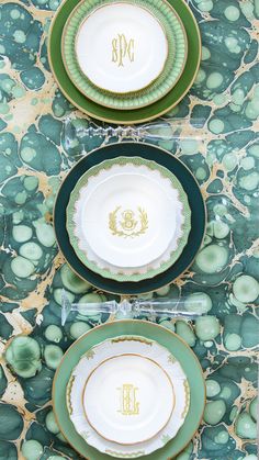 three plates with monogrammed green and gold trim on them, sitting next to each other