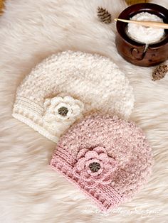 two knitted hats sitting on top of a white fur covered floor next to a cup