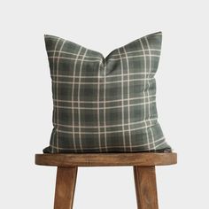 a green plaid pillow sitting on top of a wooden stool