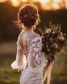 a woman in a wedding dress holding a bouquet and looking at the sun set behind her