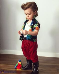 a little boy standing next to a toy parrot on top of a hard wood floor