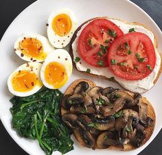 a white plate topped with an egg, toast and mushrooms next to spinach leaves